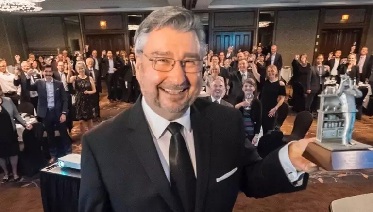 Celebrating a Pillar of Pharmacy | Picture of Marshall Moleschi holding his award in front of a crowd waving behind him - The Canadian Foundation For Pharmacy