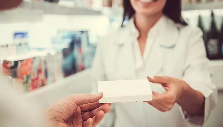Cost-effectiveness of UTI prescribing attracts attention | Picture of female pharmacists handing over a prescription box to with no label to patient - The canadian Foundation For Pharmacy