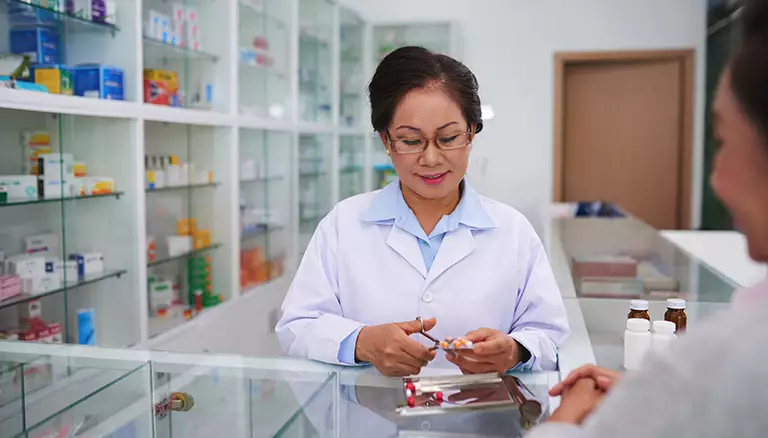 Deprescribing, within a pharmacist's domain | Picture of female asian pharmacist cutting down the amount of capsules in a prescription - The Canadian Foundation For Pharmacy