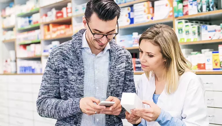 Picture of a female pharmacist talking to a young men who is checking a prescription on his mobile phone - The Canadian Foundation For Pharmacy