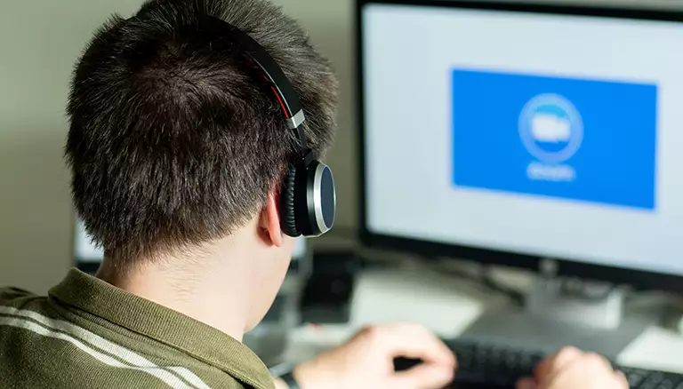 CFP Pharmacy Forum tackles impact of COVID-19 | Picture of man wearing headphones looking at a computer screen with the Zoom logo on it - The Canadian Foundation For Pharmacy