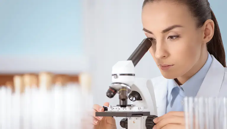 CFP/AFPC Graduate Student Award | Picture of young woman in white lab coat looking through a microscope - Canadian Foundation for Pharmacy